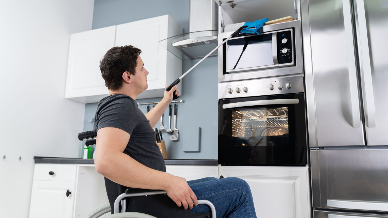 Disabled man using grabber tool to grab potholders in kitchen