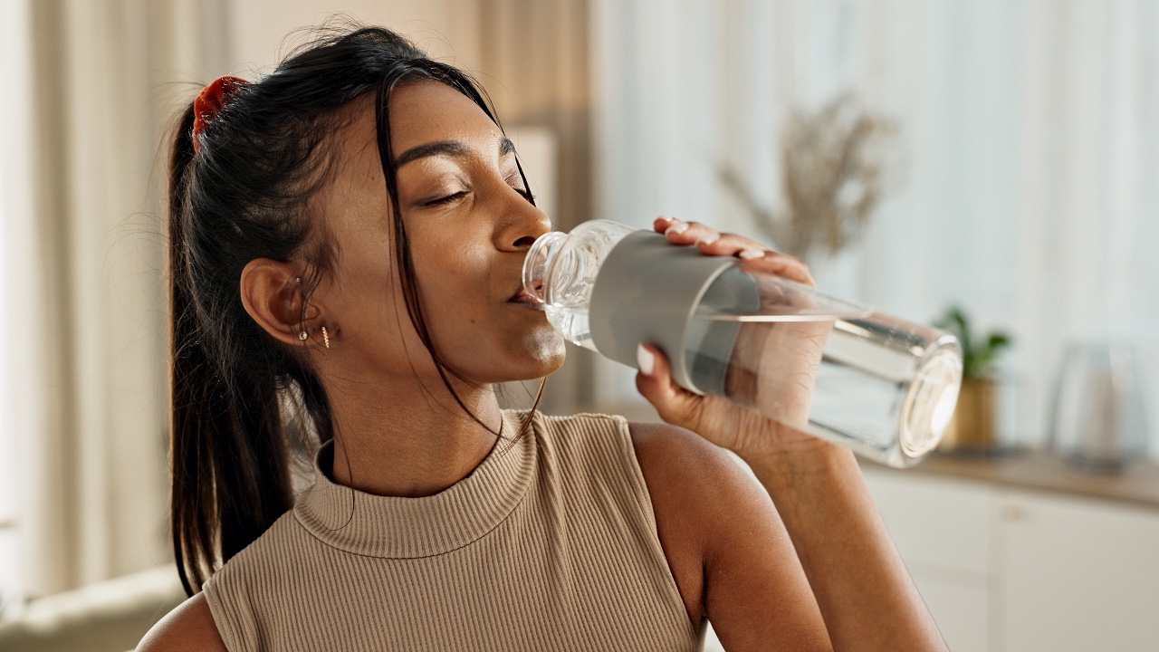 Drinking water, yoga or Indian woman in home with health, fitness or wellness for natural hydration. Thirsty female person, tired or healthy girl with liquid bottle after pilates to detox or relax