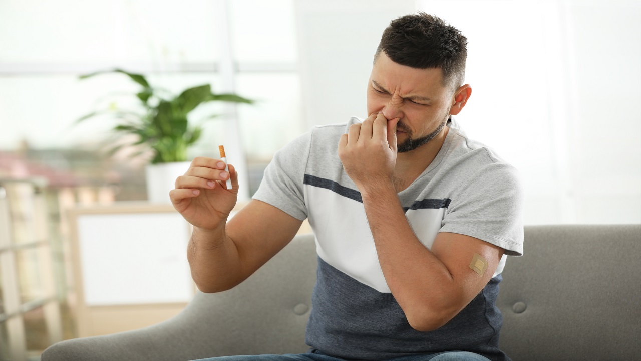 Emotional man with nicotine patch and cigarette at home couch, quit, no smoking