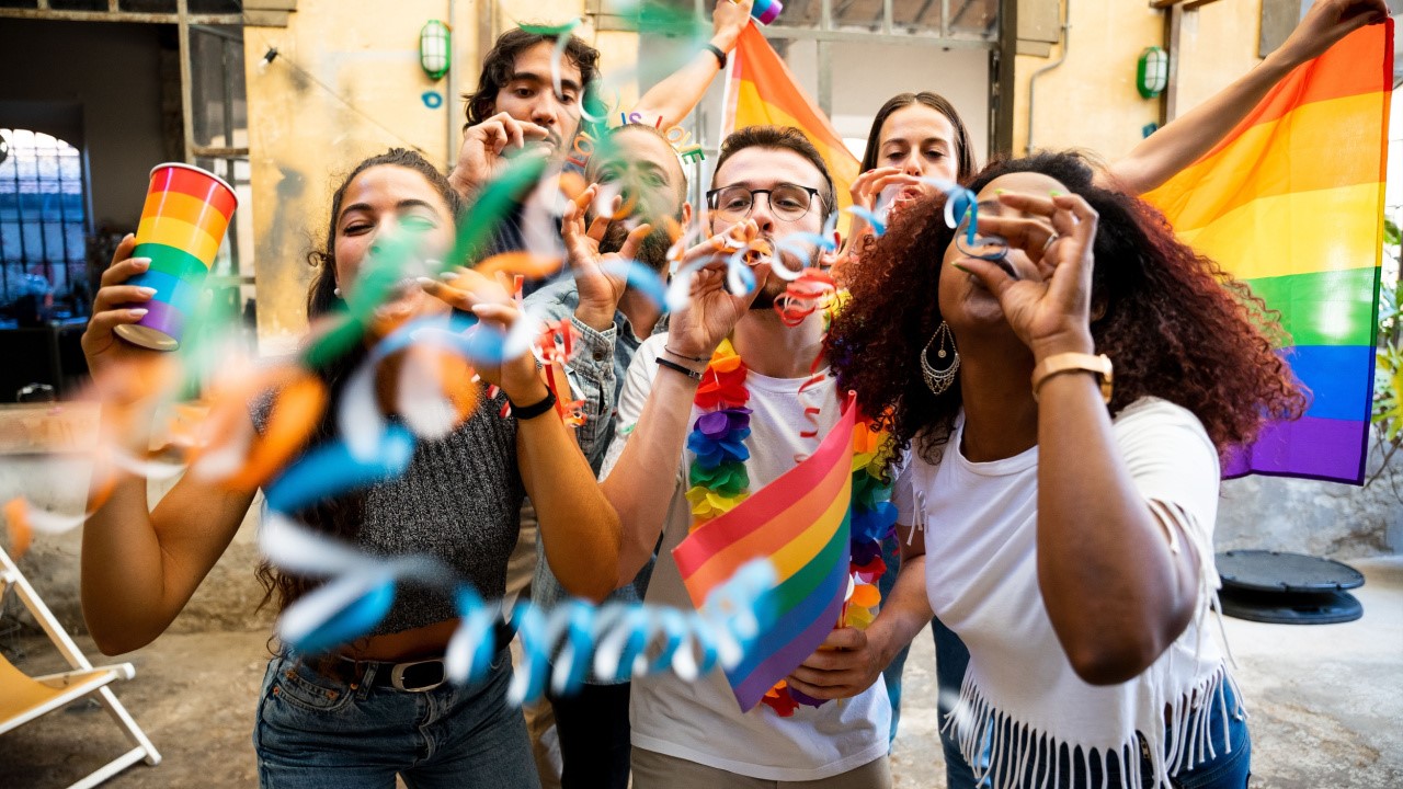 Friends celebrate with flags and festive streamers by dancing and blowing off round dot streamers