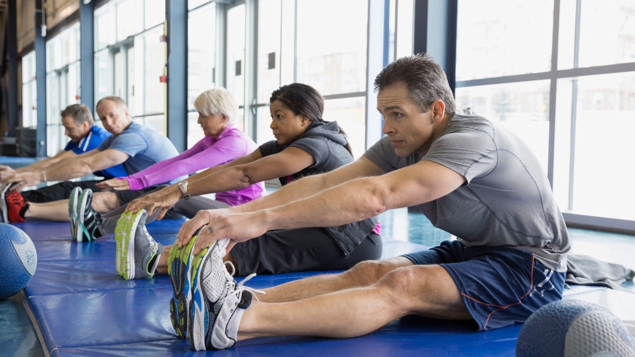 Group stretching in exercise class at gym, sit and reach workout session