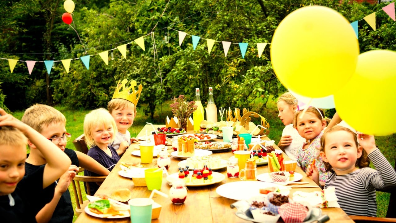 Kids celebrating at a birthday party with hanged paper bunting, flags and baloons