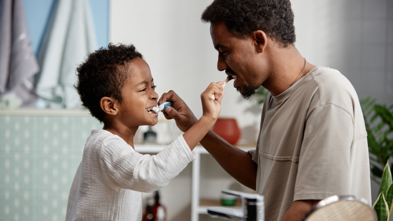 Little Black boy and father brushing each others teeth, toothbrush fun together in bathroom