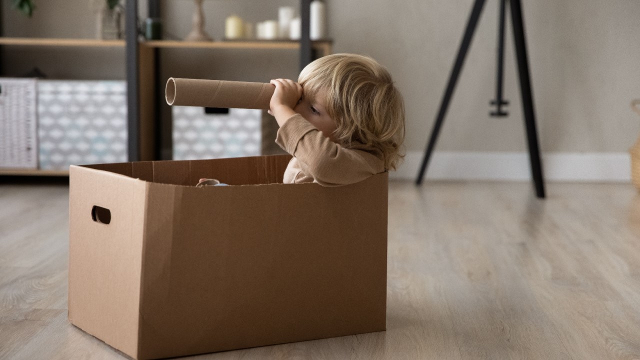 Little preschool boy playing sailor, looking through tube paper toy spyglass tube from cardboard box and papers