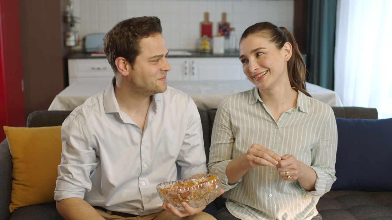 Married couple eating mixed nuts while sitting on the couch, eating hazelnuts, peanuts, almonds, watch movies on TV and fun