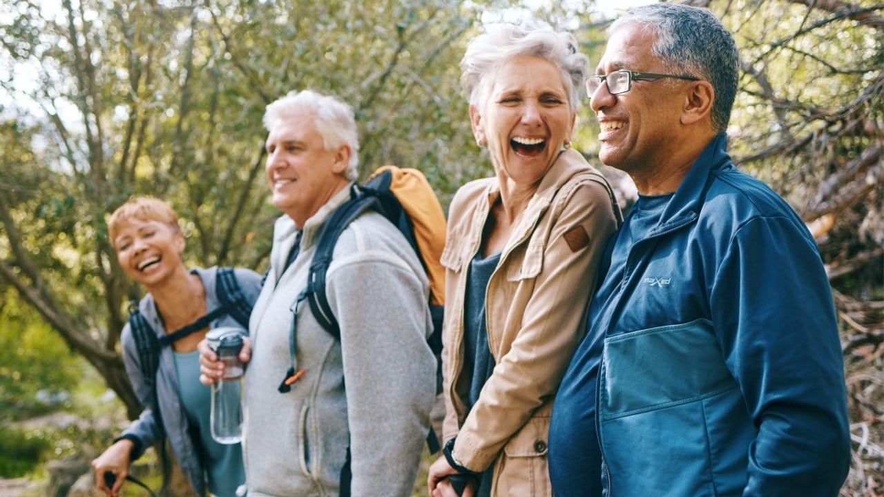 Nature, hiking and happy senior friends bonding, talking and laughing at comic joke in forest. Happiness, fun and group of elderly people trekking together for health, wellness and exercise in woods.