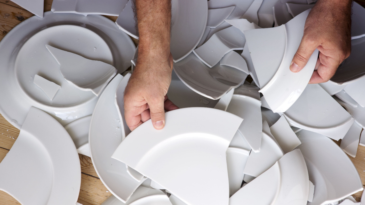 Plates smashing, hands picking up broken white plates from wooden floor