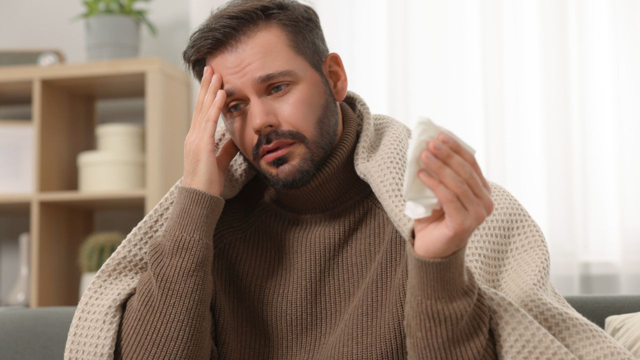 Sick man with tissue wrapped in blanket on sofa at home