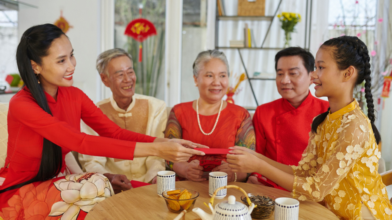 Smiling mother giving lucky money envelope to her teenage daughter at Tet celebration, red envelope tradition