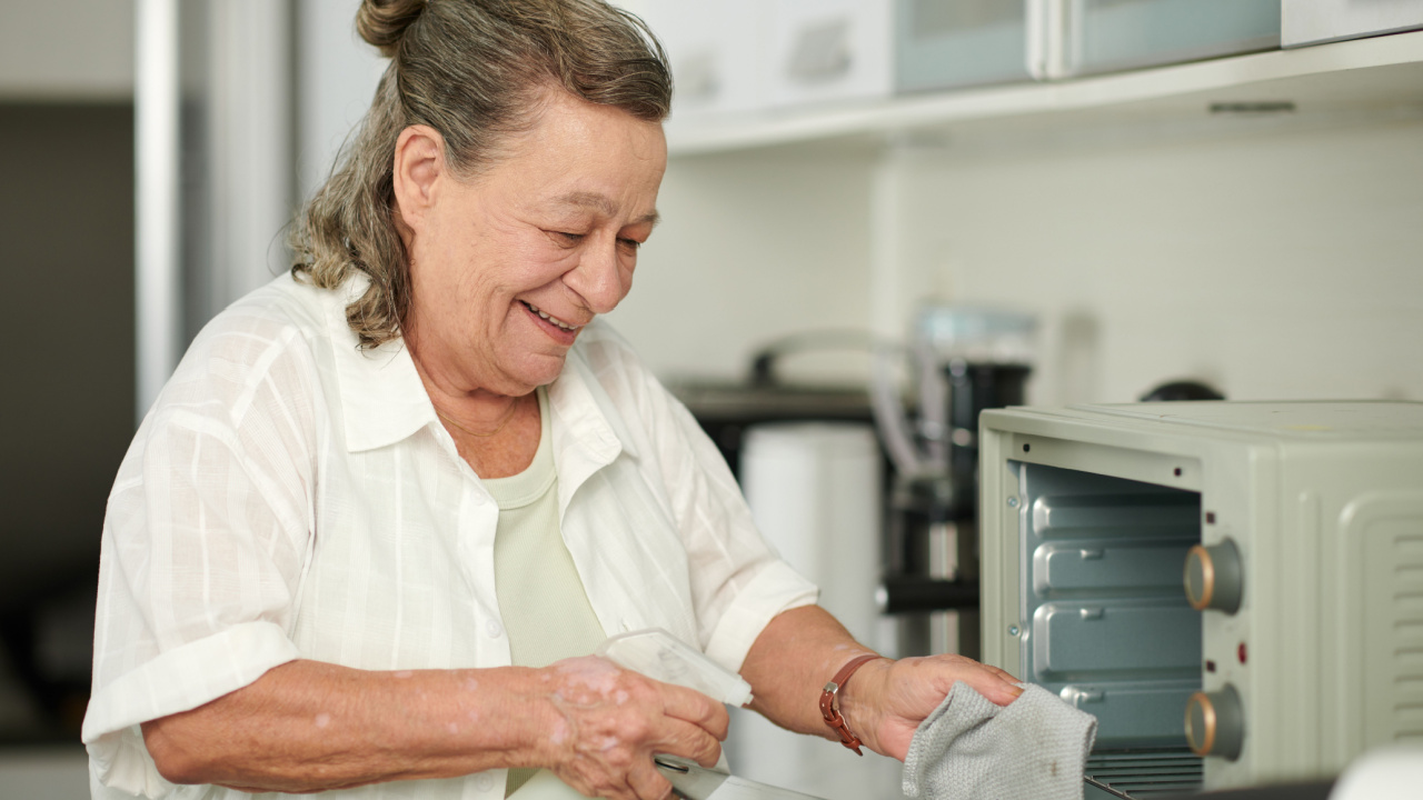 Smiling senior woman cleaning microwave with detergent, removing grease and stains