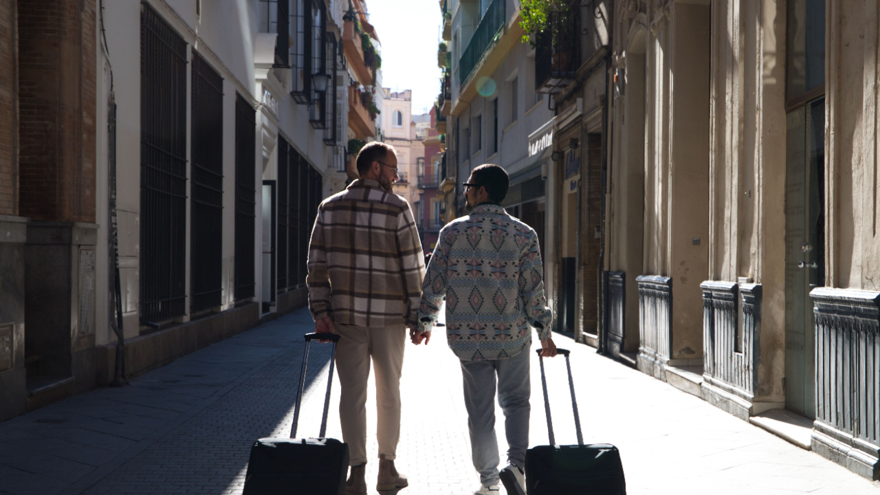 Two male friends walk down a street with their suitcases as they embark on a travel jouney