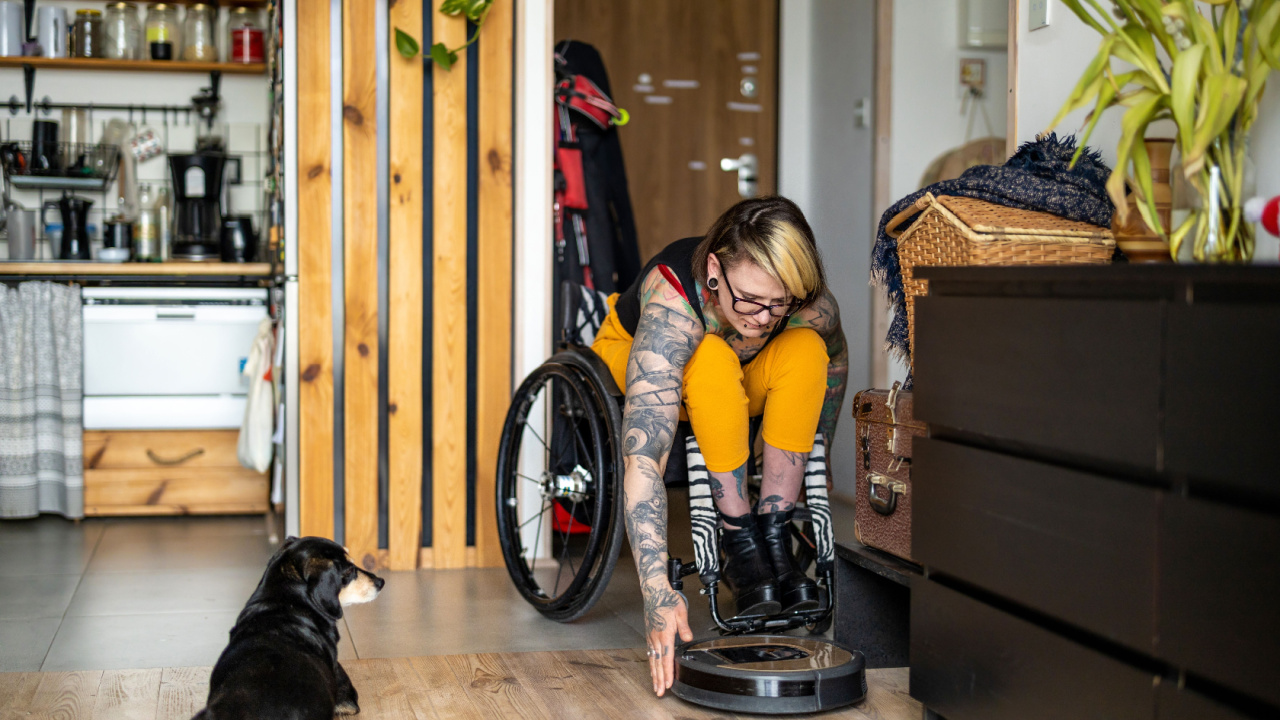 Woman in wheelchair adjusting smart robot cleaner, robot vacuum cleaner at home