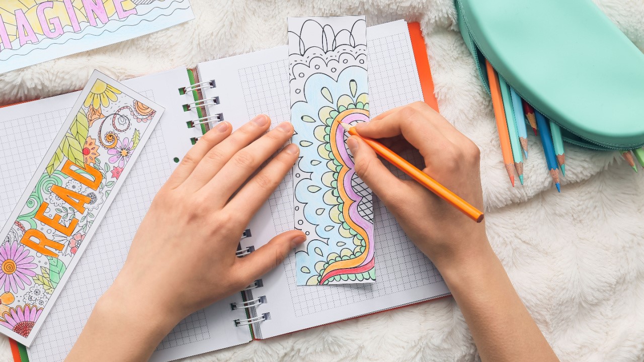 Woman making and coloring bookmark made of papers on bed