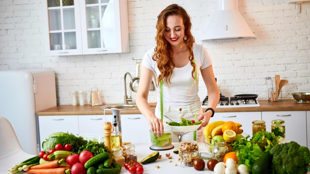 Young happy woman preparing tasty salad in the beautiful kitchen with green fresh ingredients indoors. Healthy food and Dieting concept. Loosing Weight