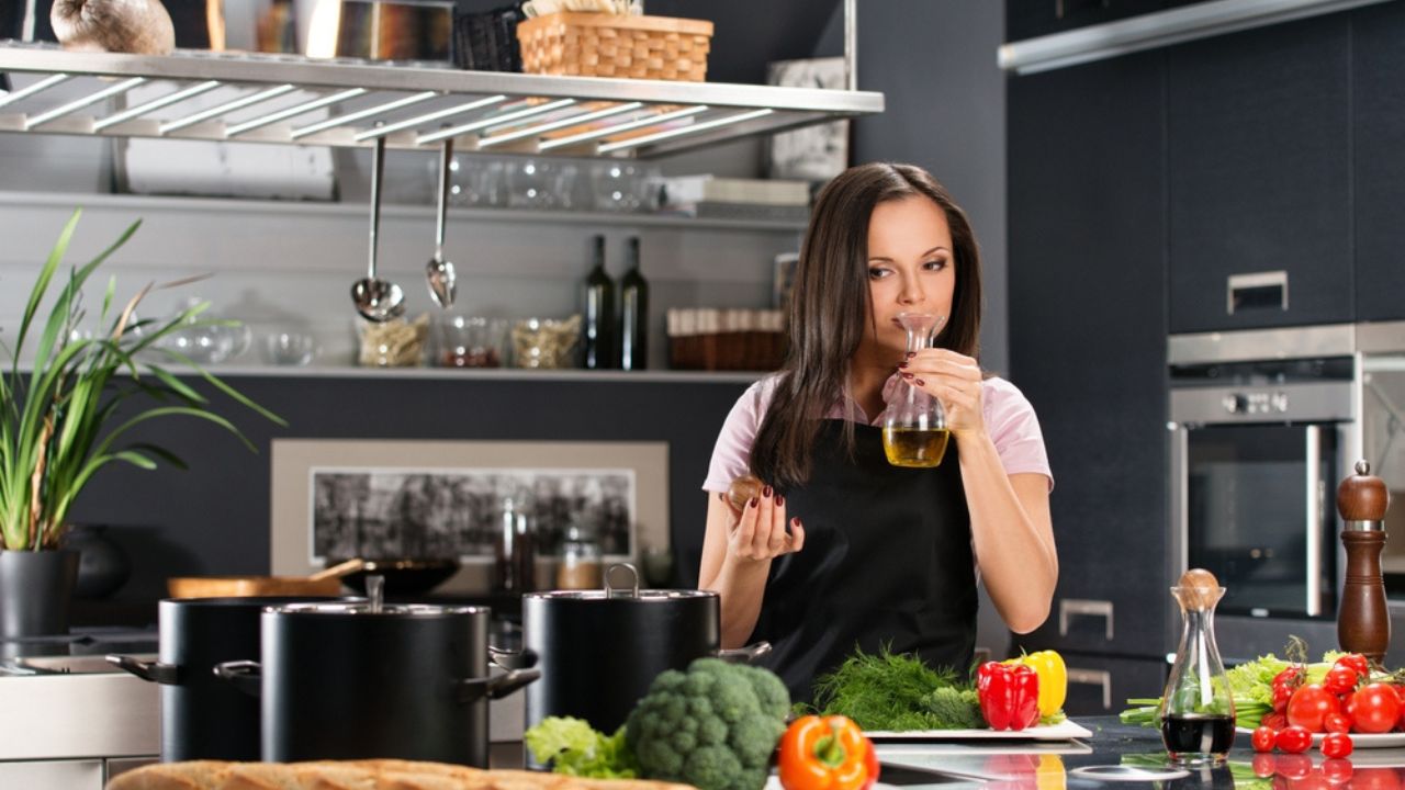 Young woman in apron on modern kitchen smelling olive oil