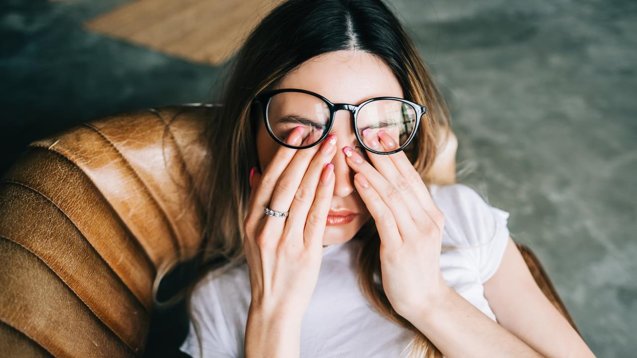 Young woman rubs her eyes after using glasses. Eye pain or fatigue concept.