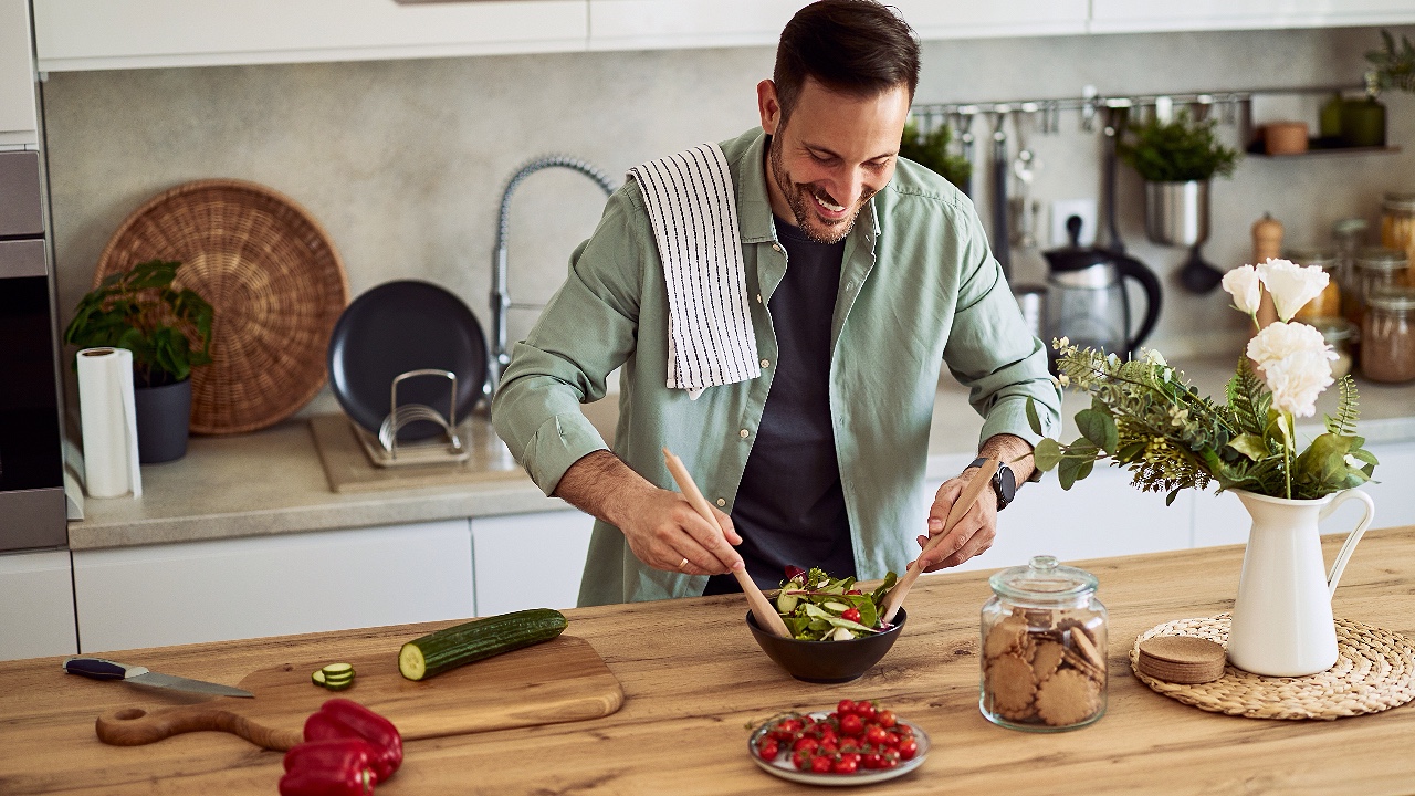 cheerful home male chef mixing a bowl of fresh and healthy vegetable salad on a kitchen counter